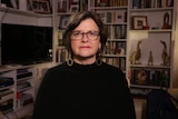 A woman wearing glasses with a bookcase behind her.