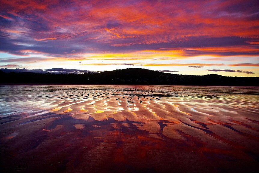 Vibrant colours of the setting sun reflect on the water-logged sand during low tide.