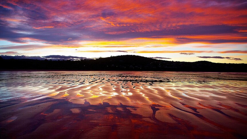 Vibrant colours of the setting sun reflect on the water-logged sand during low tide.