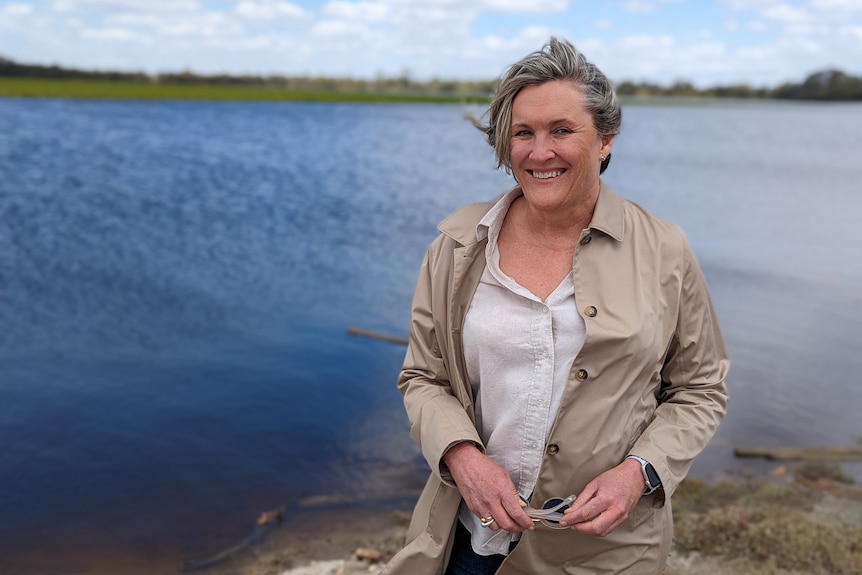 Lyndall Rowe, a white woman with short grey hair stands in front of a flooded vineyard.