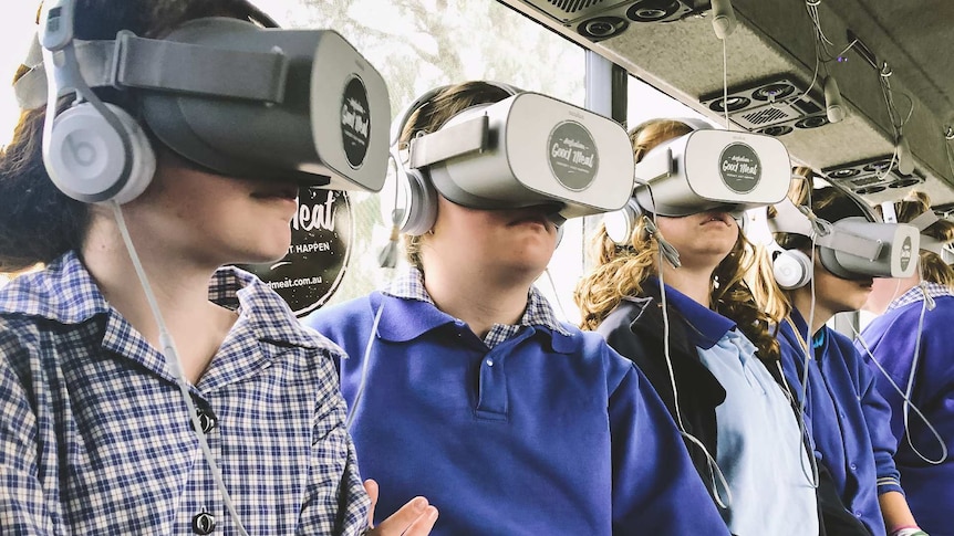 Five girls in school uniform wearing virtual reality goggles within a specially equipped bus.