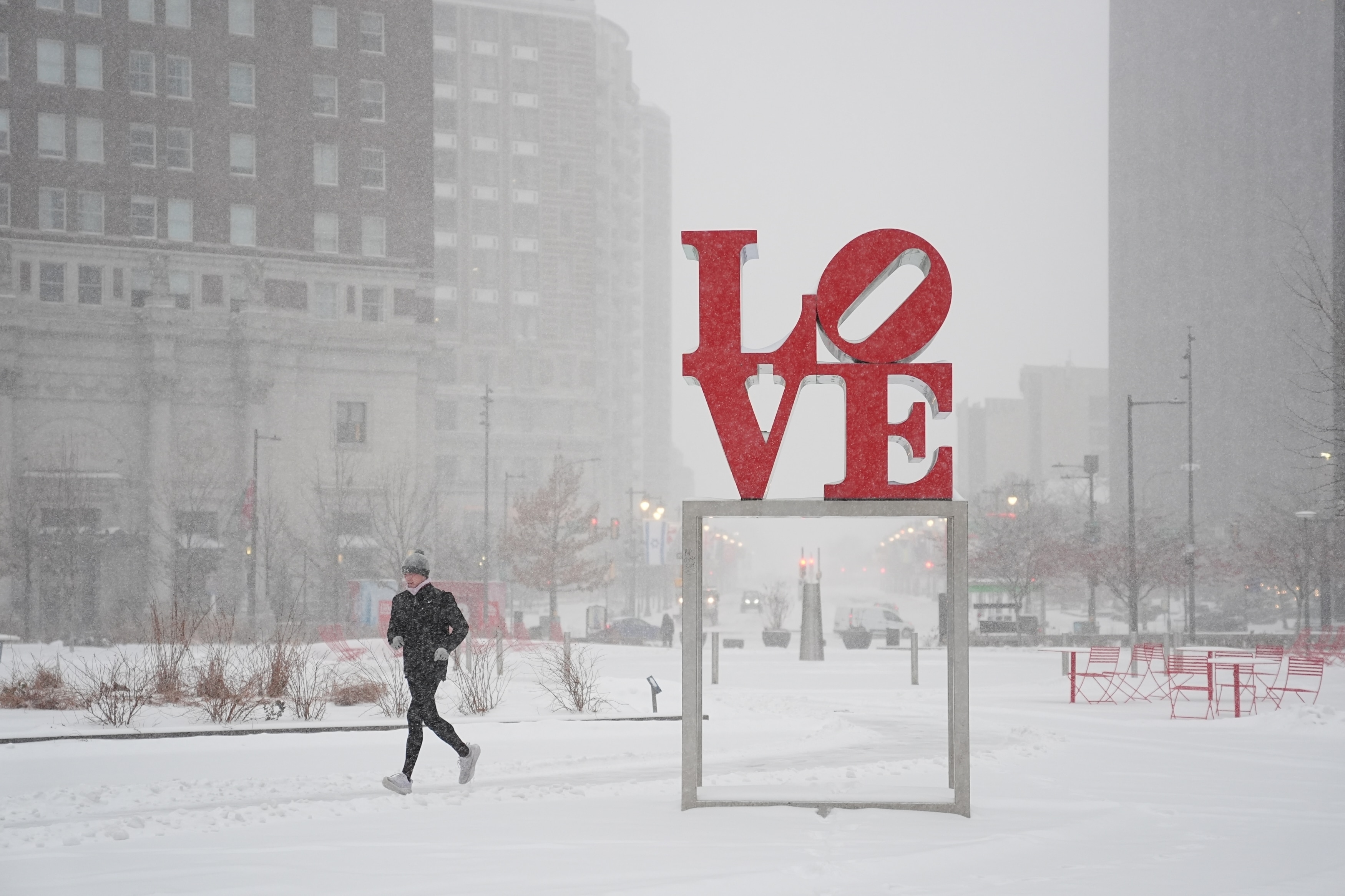 Una persona hace jogging mientras nieva junto a un cartel rojo que dice 