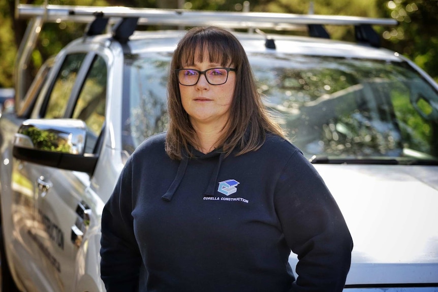 Ella Brown in dark blue Corella Construction sweat shirt, standing in front of a silver ute.