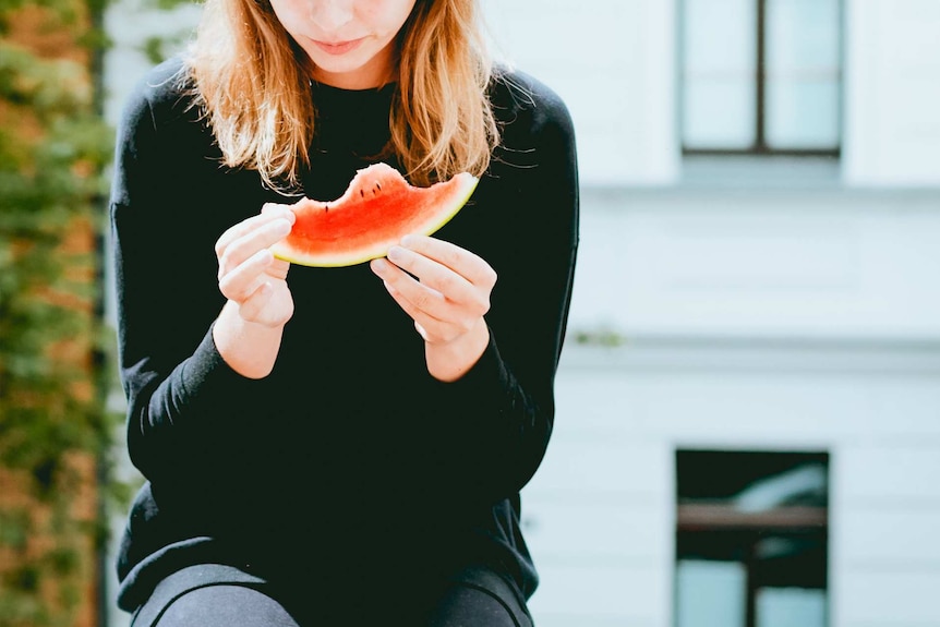 Woman looking at a slice of watermelon to depict an article about disordered eating thoughts and behaviours