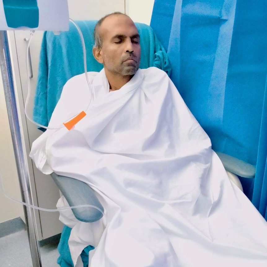 A man sits in a hospital chair with his eyes closed.