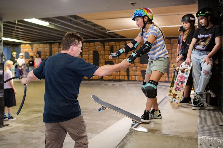 Ando holds a girl's hand as she readies herself to drop in.