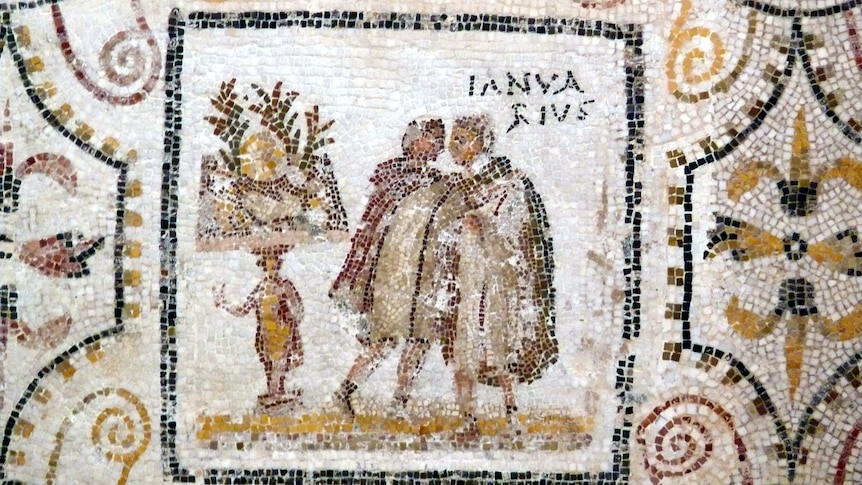 A Roman mosaic showing two men in robes standing next to a table bearing plant decorations, with the inscription 'Ianuarius'.
