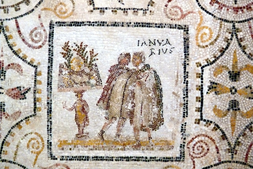 A Roman mosaic showing two men in robes standing next to a table bearing plant decorations, with the inscription 'Ianuarius'.