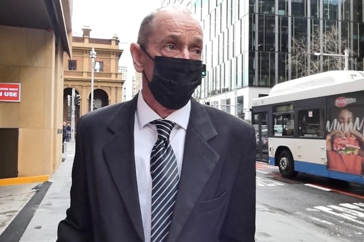 A man in a suit walks along a street wearing a face mask