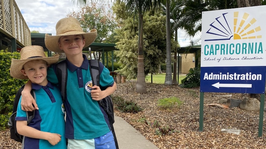 Two boys wearing cowboy hats standing at a school. There is a Capricornia school of distance sign near them