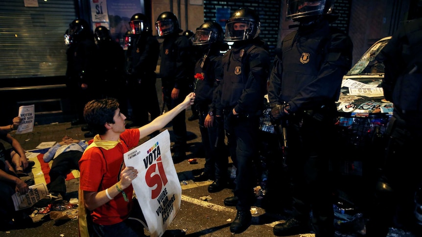 A protesting man holds out a carnation to a row of armed police officers