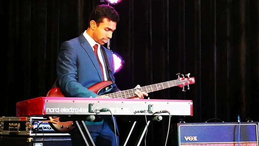 Musician Gana Aruneswaran performing on stage with keyboard and bass guitar.