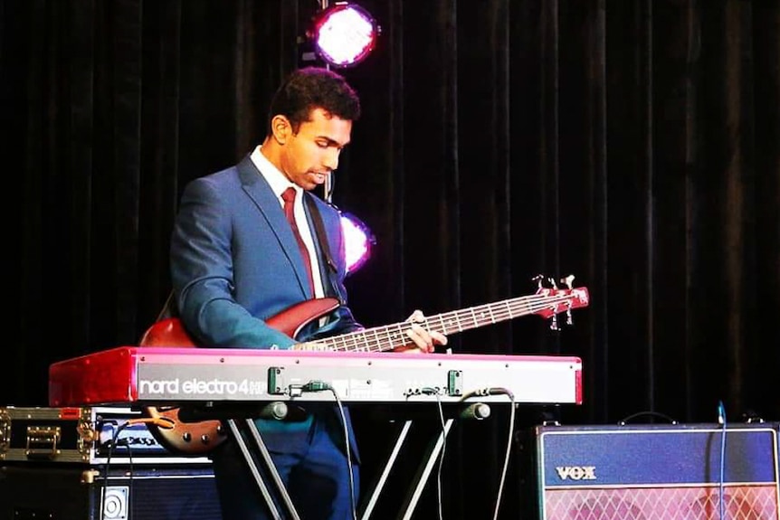Musician Gana Aruneswaran performing on stage with keyboard and bass guitar.