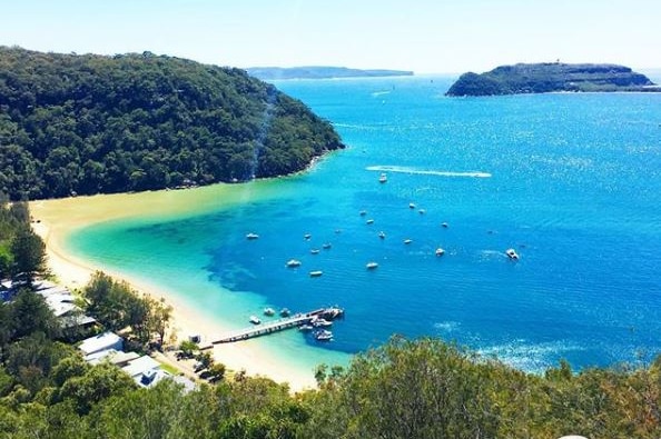 A coastal outlook shows a number of boats approaching a jetty. An islands peeks out from the edge of the frame.