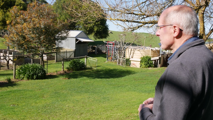 A man looks out over property to a shed, compost bins, sunken water tanks and lush, green grass