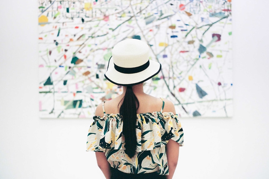 A woman looks at an abstract artwork on a white wall.