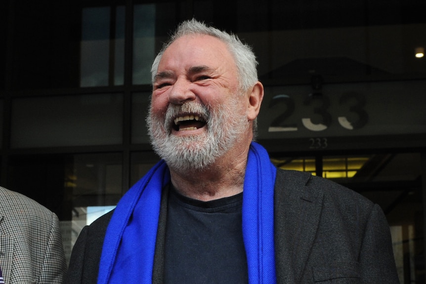 Les Twentyman laughing with a blue scarf around his neck.