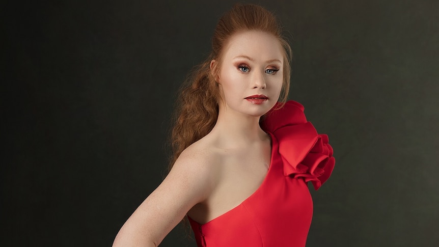 Maddie in a red dress with hair half up and down, posing towards the camera.