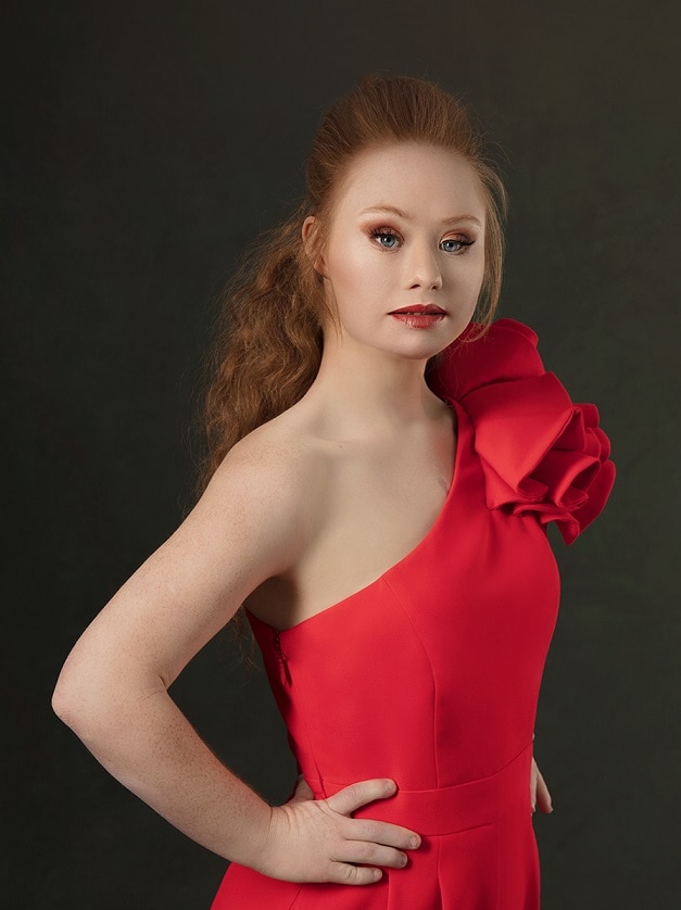 Ms Stuart in a red dress with hair half up and down, posing towards the camera.