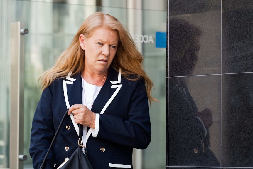 A woman in a dressed in a navy blue jacket walks out of a court building