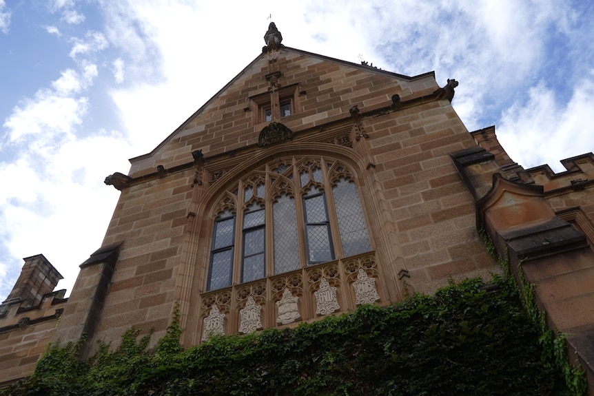 A sandstone neogothic building under a blue sky with white clouds.