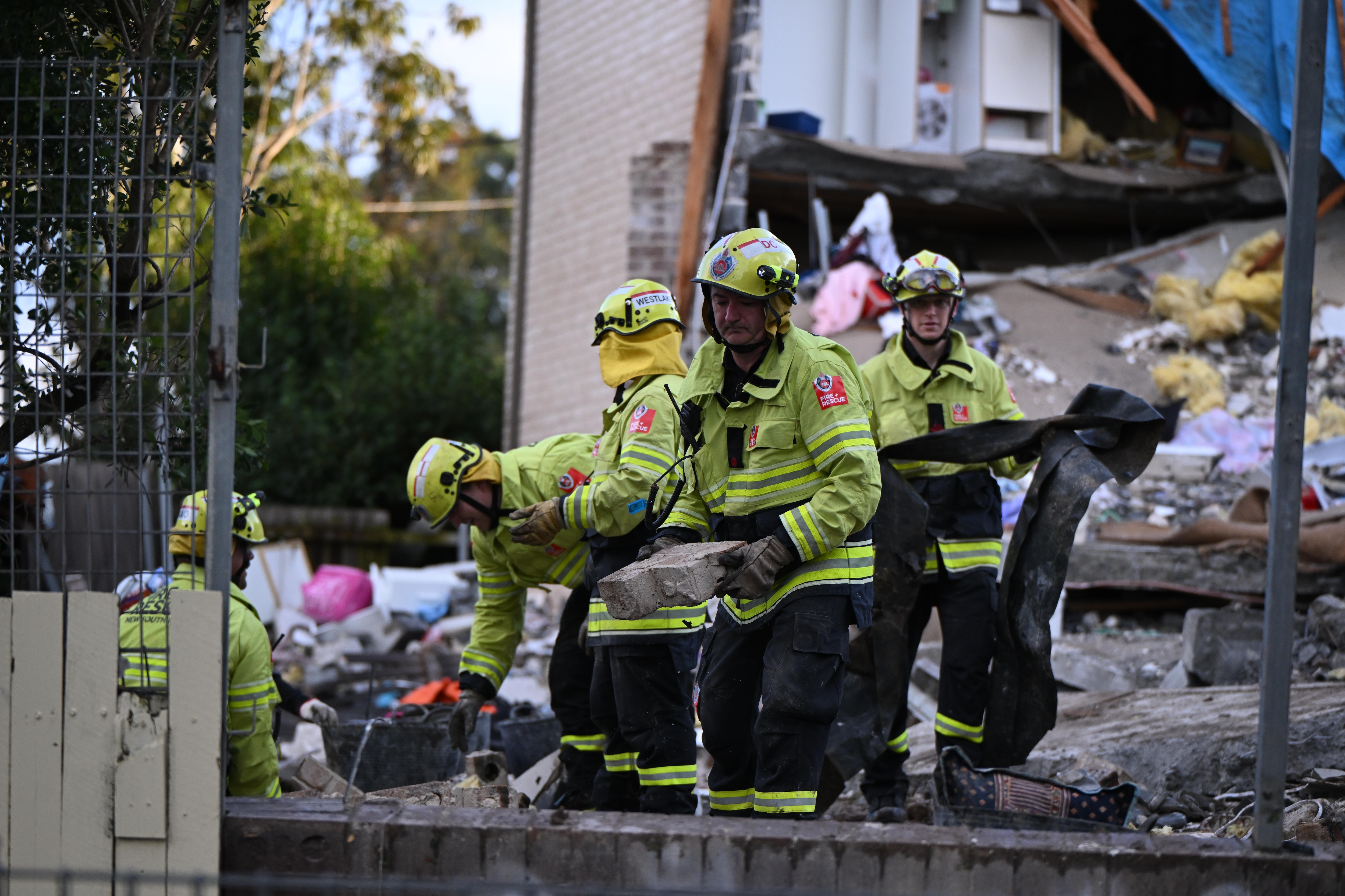 Emergency workers dressed in hi-vis yellow attend to an exploded house