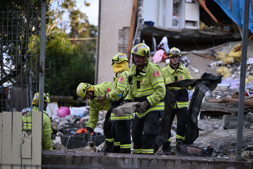 Emergency workers dressed in hi-vis yellow attend to an exploded house