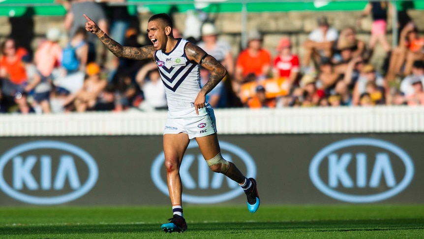 Michael Walters points his finger to the sky in celebration of kicking a goal.