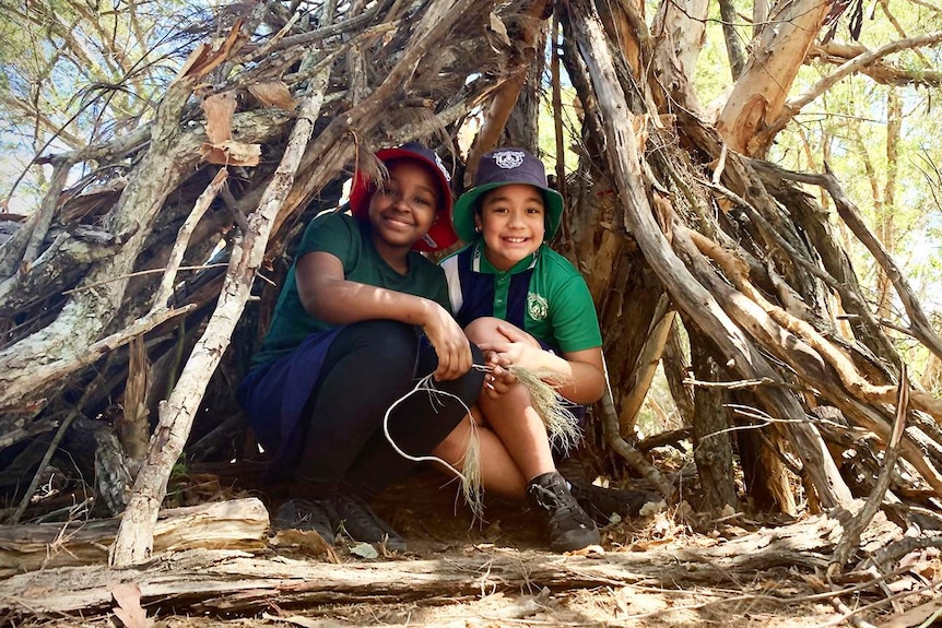 Two primary school students at Berrinba East State School sits inside a teepee they have helped make out of tree branches.