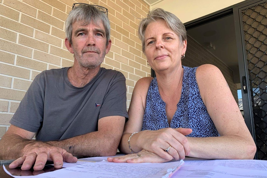 A couple sitting together at a table looking down at a camera with documents in front of them