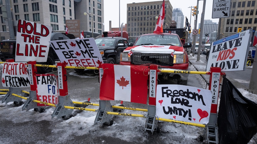 Signs sit on a barricade in front of parked vehicles as part of the trucker protest.