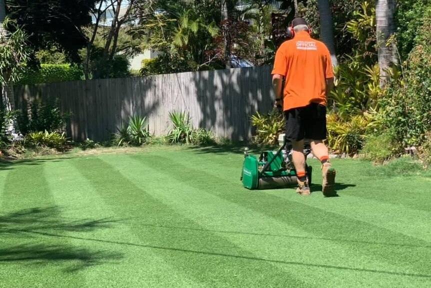 Man mowing lawn with a roller mower.