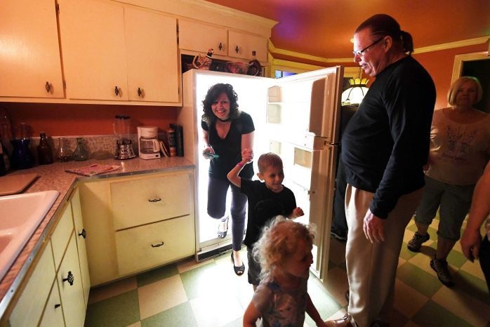 A woman holds a child's hand as she step out of a fridge into a kitchen.