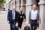 Two men and a woman, all lawyers, walking into a courthouse with briefcases.  