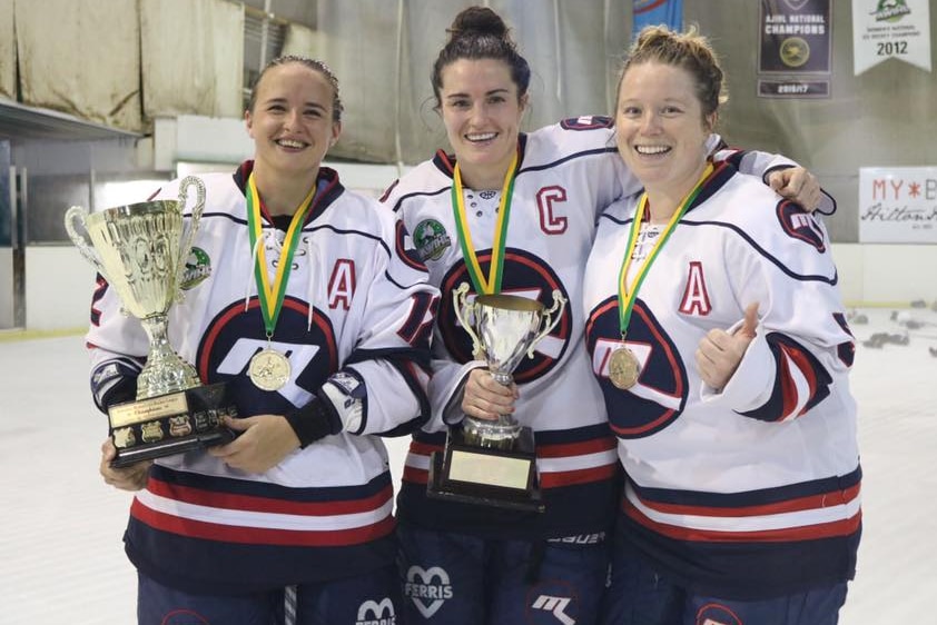 Georgia Moore and Christina Julien smile standing with one of their teammates after winning the Women's Ice Hockey League.