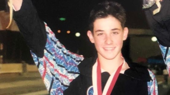 A teenager in a sports tracksuit wearing a medal and holding a bouquet.
