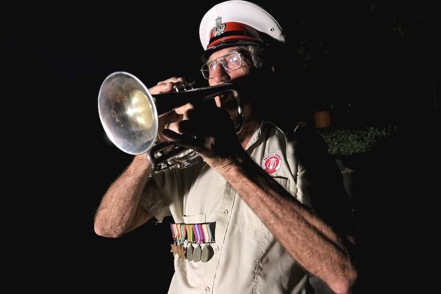 A man in uniform playing a cornet in the pre-dawn darkness
