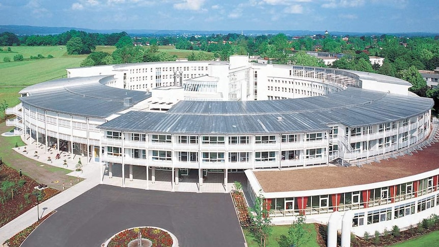 A large circular hospital building in Germany centred 50 kilometres from Munich, bordering a large green field.