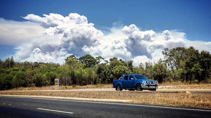 A picture taken from a moving vehicle of a giant plume of thick white smoke billowing into the sky.