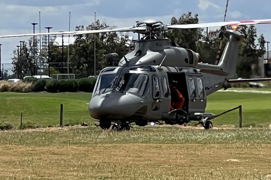 A helicopter on the grass with workers visible at the doorway.