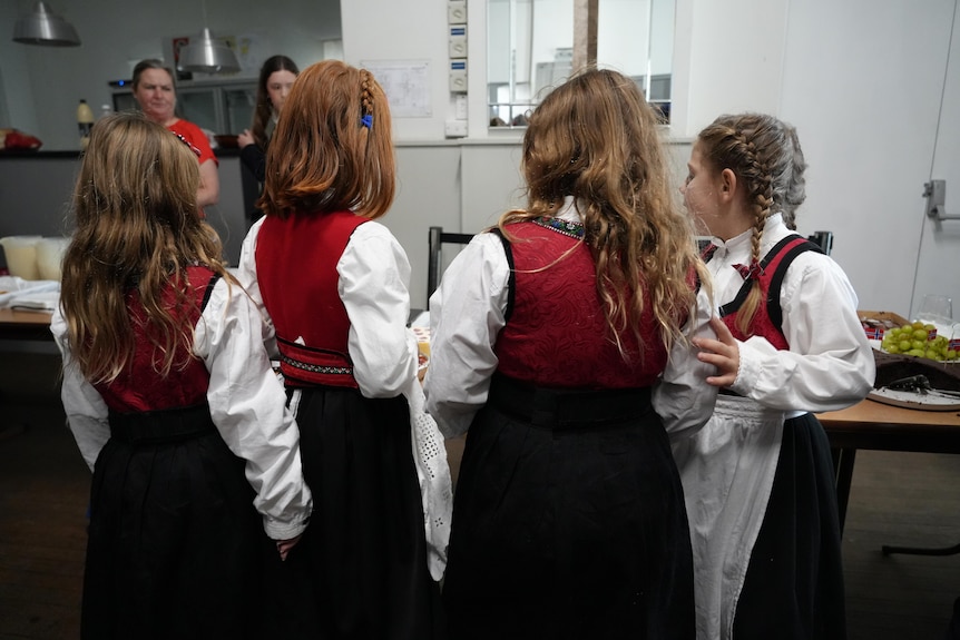 Four girls have their backs turned to the camera and are dressed in traditional Norwegian outfits.