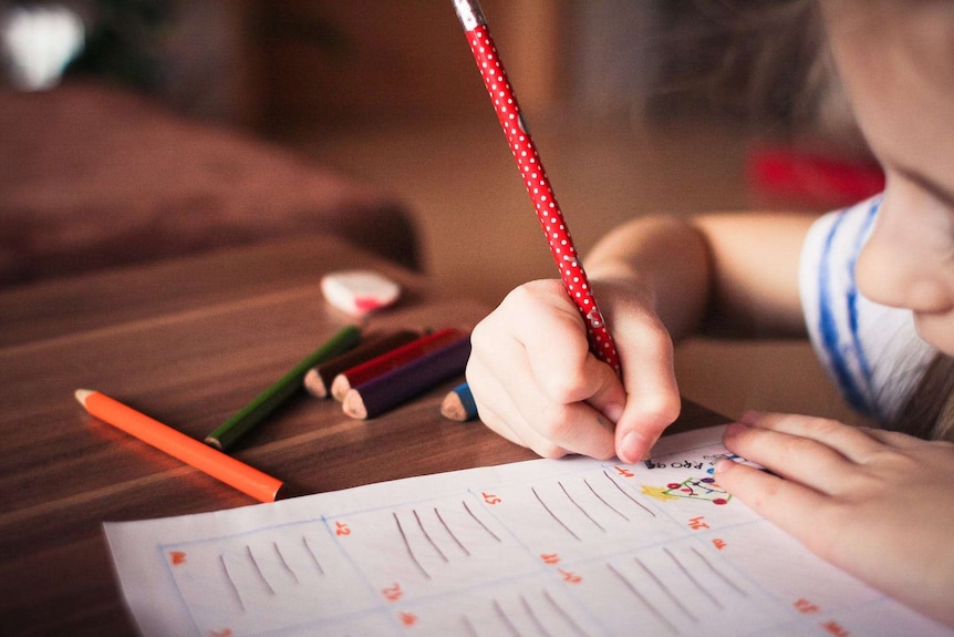 An unidentified girl writes on a piece of paper with a pencil.