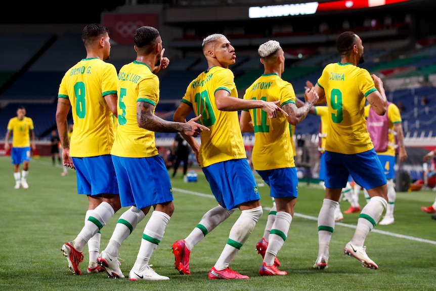 Five men wearing yellow shirts and blue shorts stand in a line