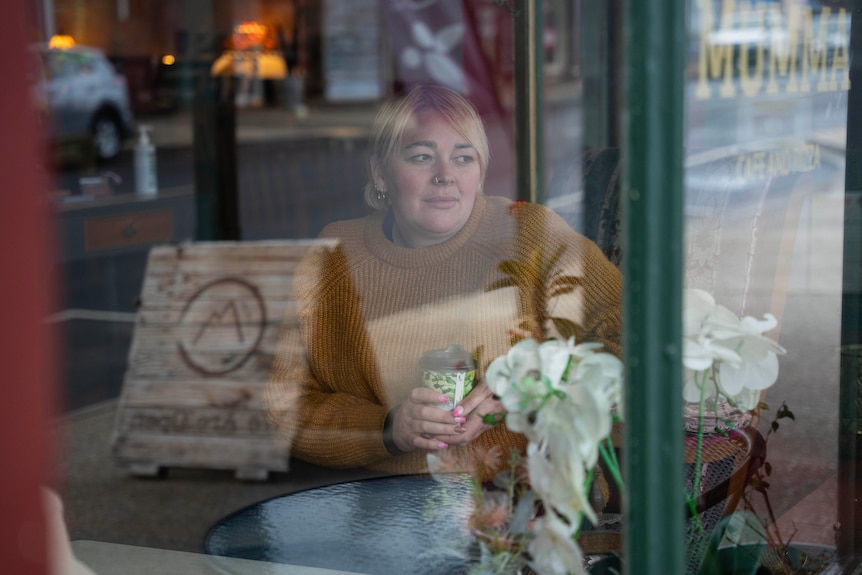 A woman looks out the front window of a cafe.