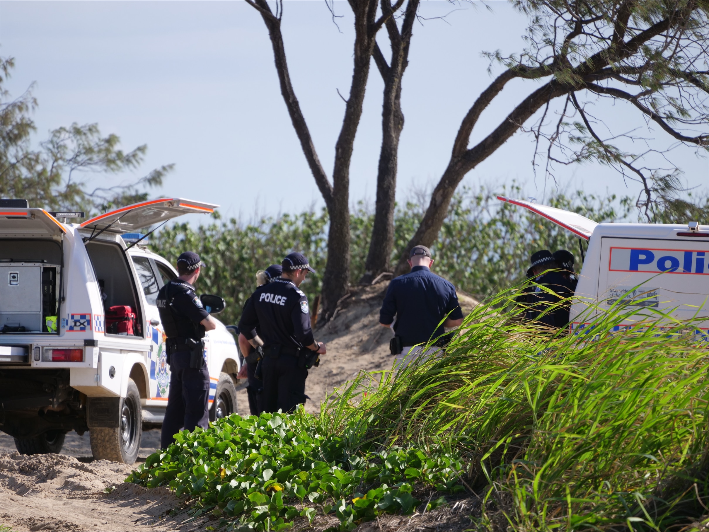 Police officers standing near vehicles at a beach.