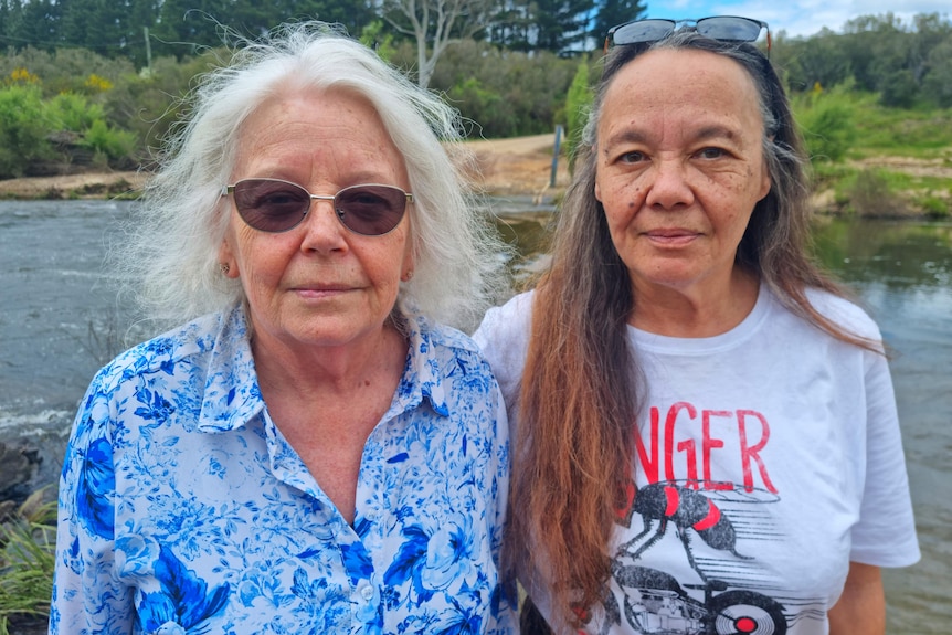 Helen and Julie smile at the camera, standing in front of a river.