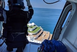 A CareFlight rescue worker is seen poised to exit an aircraft hovering over a cruise ship.