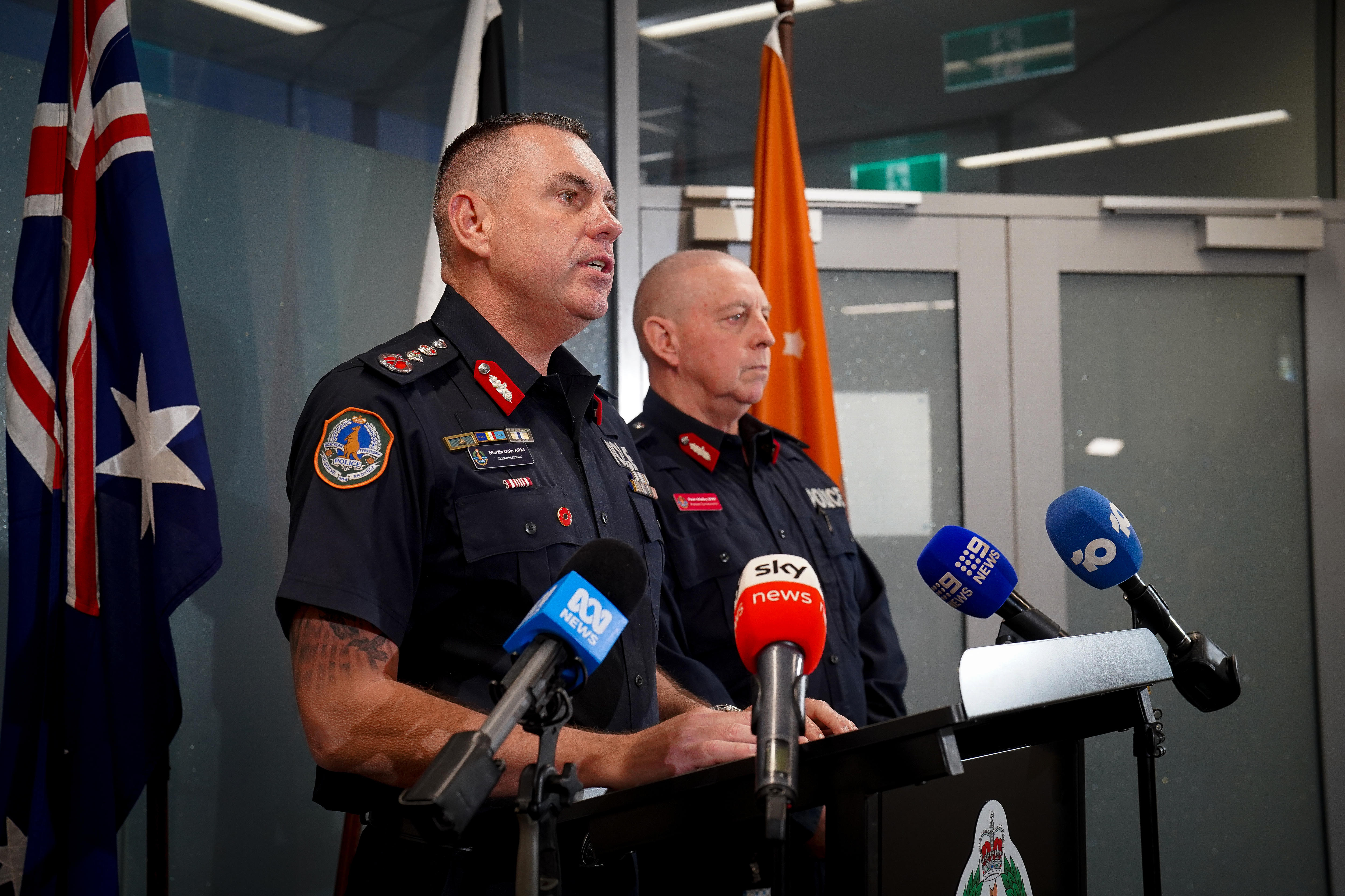 Two male police officers, looking serious, standing at a lectern and speaking into media microphones.