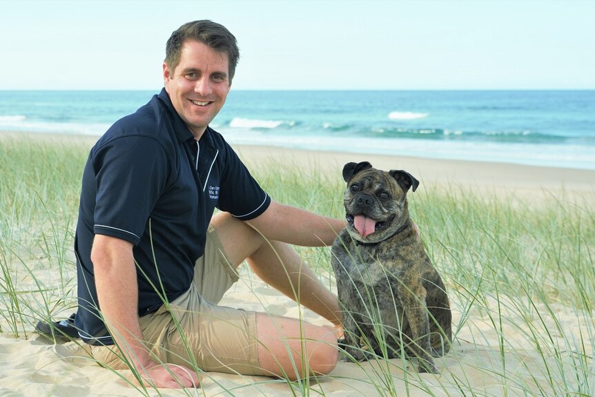 A photo of Kevin the brown mini Australian bulldog with Dr Dan Capps at the beach