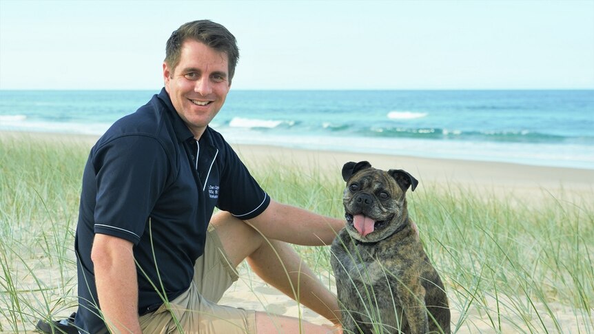 A photo of Kevin the brown mini Australian bulldog with Dr Dan Capps at the beach